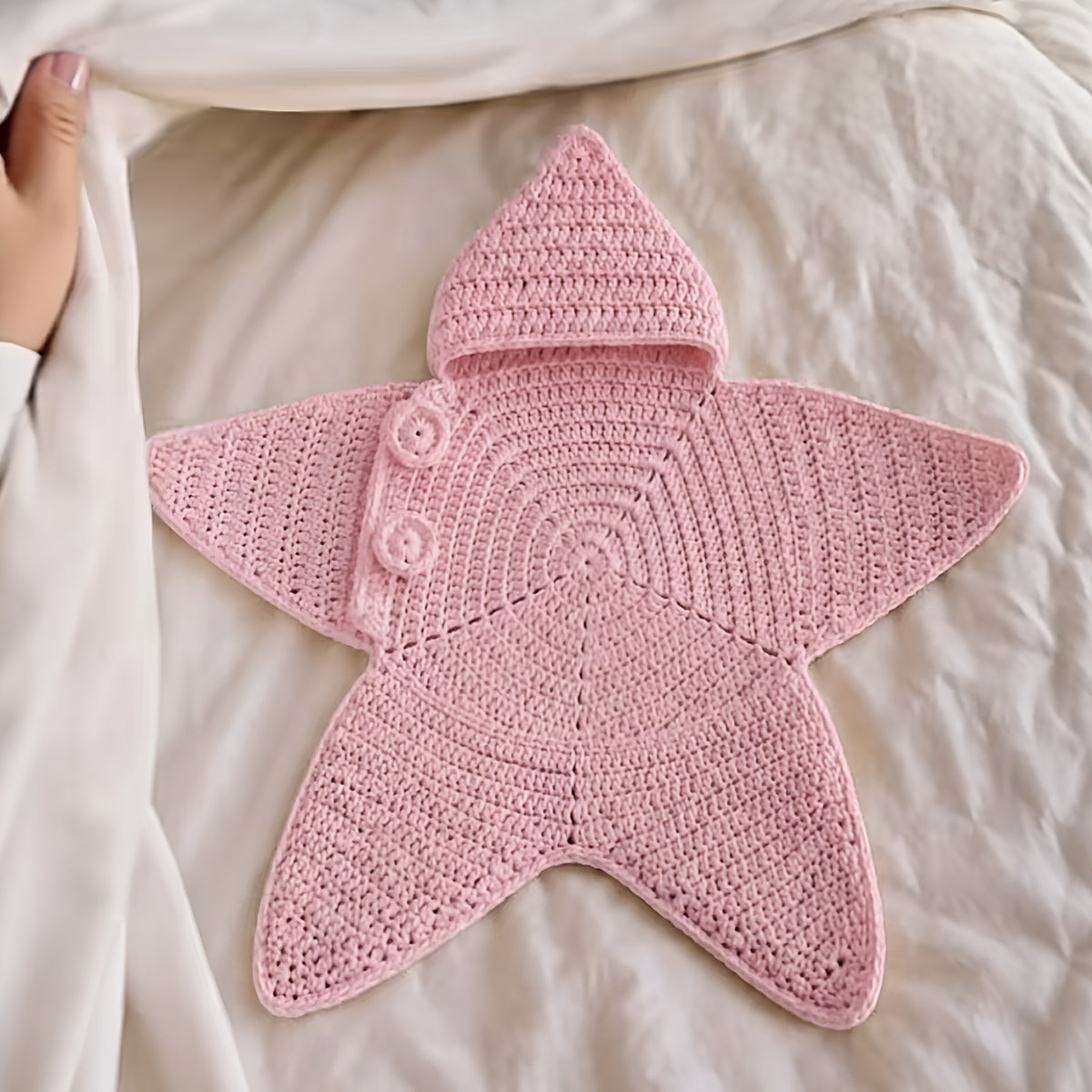 Pink hooded star-shaped crochet outfit laid flat on bedding