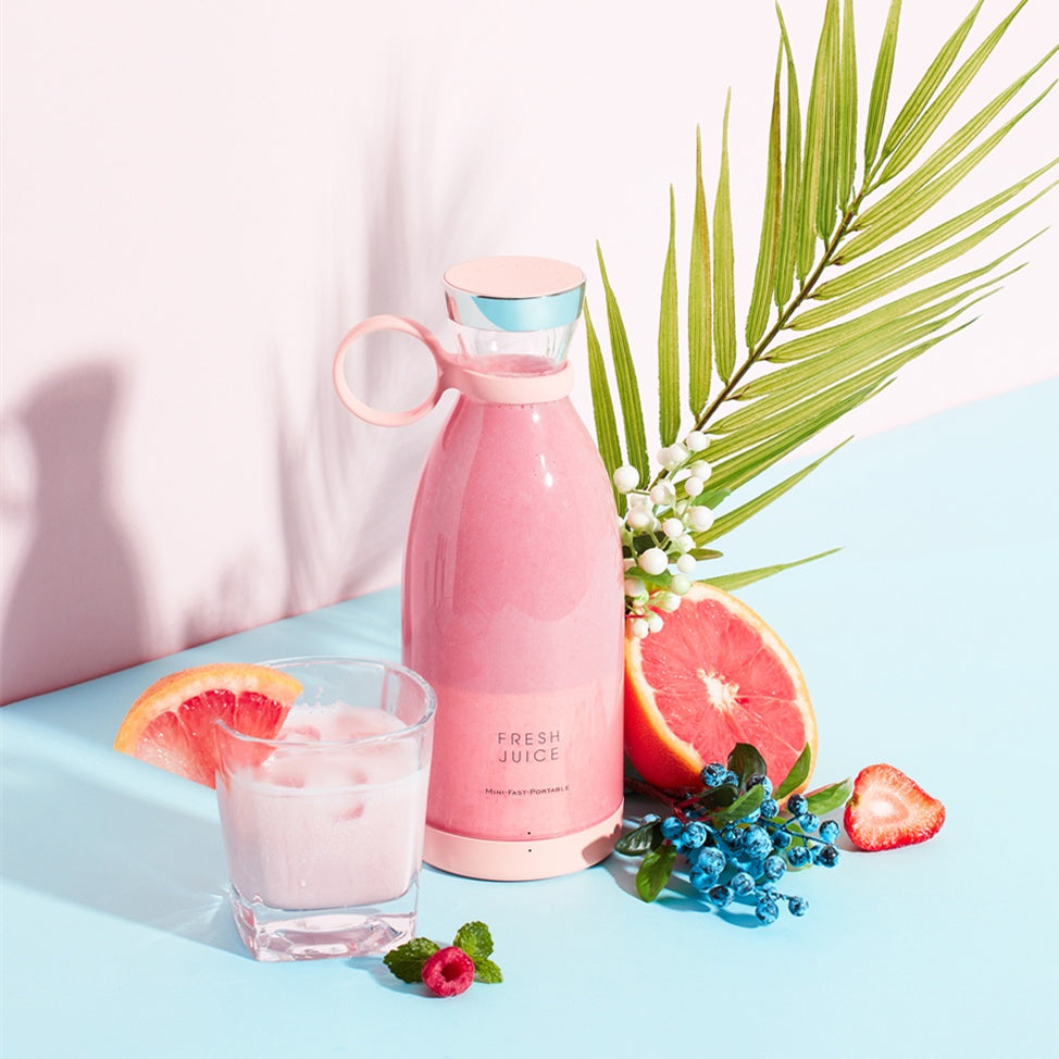 Pink portable blender bottle pictured with a smoothie, grapefruit, strawberries and blueberries